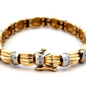 May include: A gold and silver bracelet with a textured design and small diamonds. The bracelet has a clasp closure.