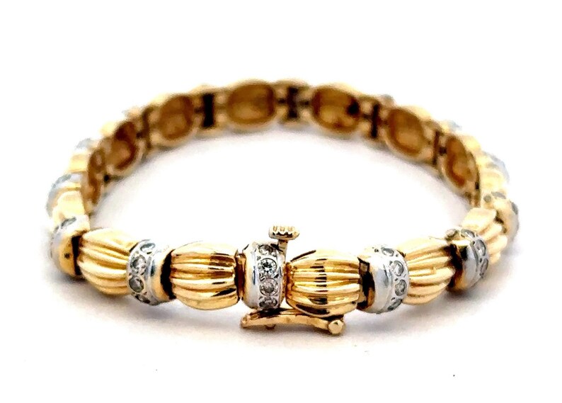 May include: A gold and silver bracelet with a textured design and small diamonds. The bracelet has a clasp closure.