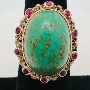 May include: A gold ring with a large oval turquoise stone surrounded by smaller pink stones.