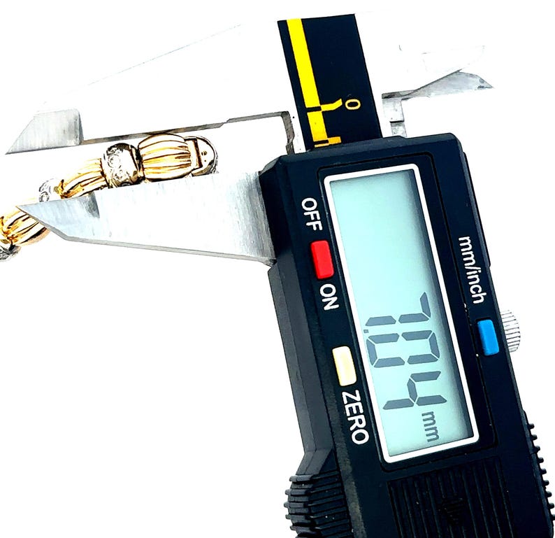 May include: A close-up of a digital caliper measuring a gold chain with a diamond accent. The caliper reads 7.04 mm.