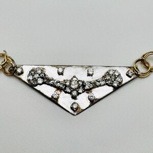 May include: A silver-toned pendant with a triangular shape, adorned with numerous small, sparkling diamonds. The pendant features gold-colored loops on each end for attachment.