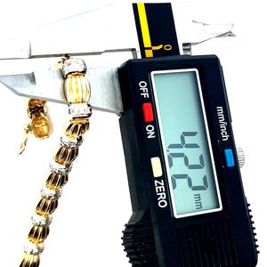May include: A close-up of a gold and white diamond bracelet being measured with a digital caliper. The caliper reads 12.2 mm.