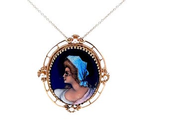 May include: Gold-toned pendant necklace featuring an oval portrait of a woman in profile, wearing a blue headscarf, set against a dark blue background. The pendant is framed with a decorative gold border and small pearls, suspended from a delicate chain.