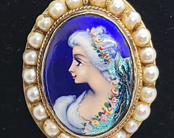 May include: A gold oval brooch with a blue enamel background and a painted portrait of a woman with a white head covering and floral accents. The brooch is surrounded by a row of white pearls.
