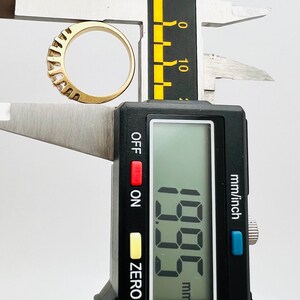 May include: A digital caliper measuring a gold ring with a row of small diamonds. The caliper reads 1.95 mm.