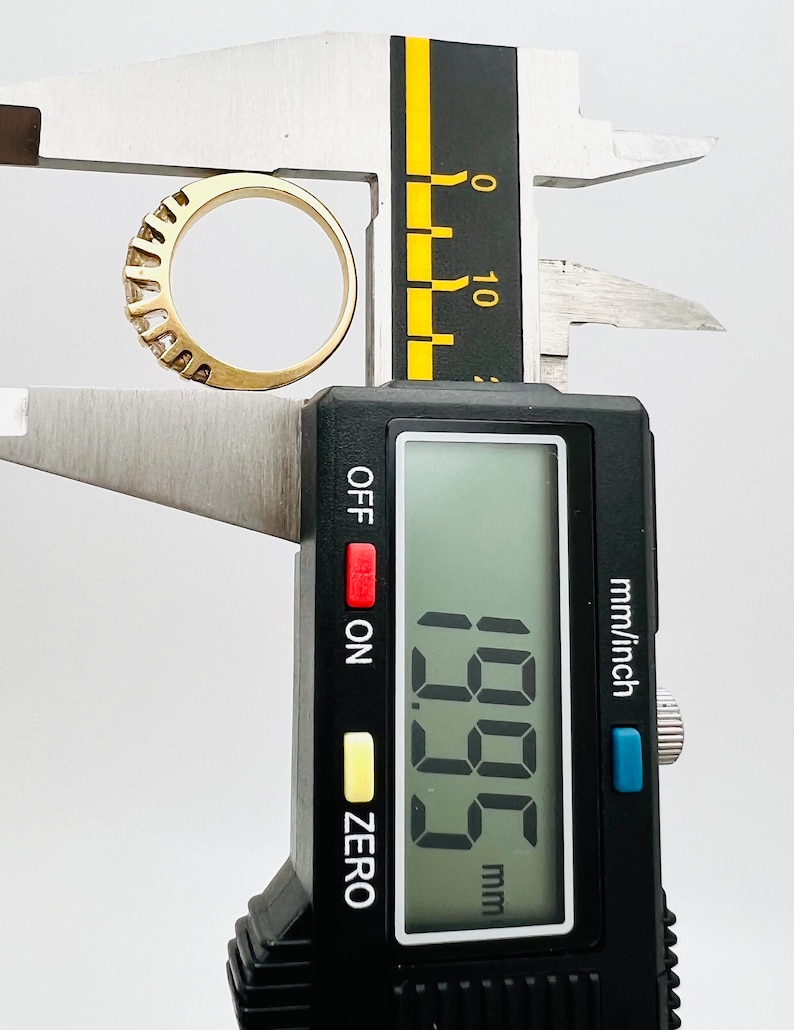 May include: A digital caliper measuring a gold ring with a row of small diamonds. The caliper reads 1.95 mm.
