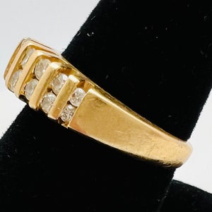May include: A gold band ring with a row of small clear diamonds set in the band.