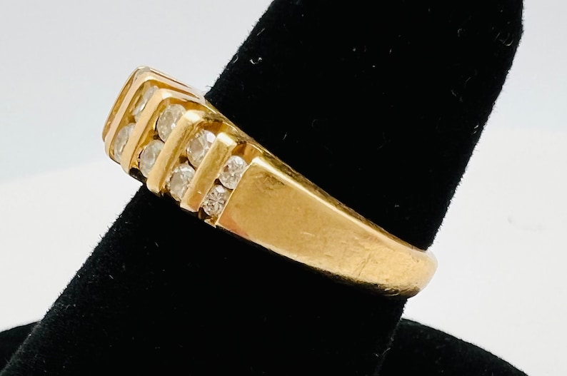May include: A gold band ring with a row of small clear diamonds set in the band.