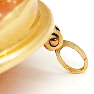 May include: A gold-toned pendant featuring a pink and white shell cameo. The pendant has a loop for attaching to a chain.