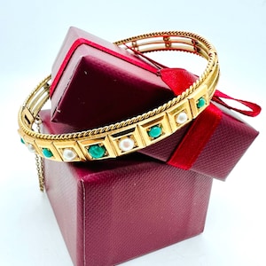 May include: A gold bangle bracelet with a rope design and alternating turquoise and pearl accents. The bracelet is on top of a red gift box.
