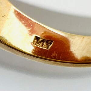 May include: Close-up of the inside of a gold ring with the hallmark "14K" stamped on the band.