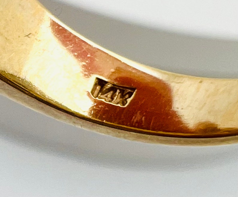 May include: Close-up of the inside of a gold ring with the hallmark "14K" stamped on the band.