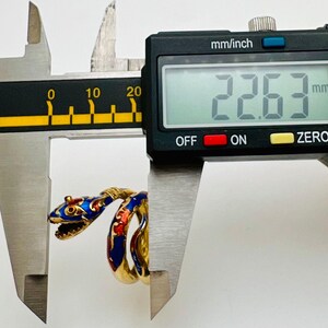 May include: A gold-colored snake ring with blue and red enamel detailing is measured with a digital caliper. The ring's head is open-mouthed, and the caliper displays a measurement of 22.63 mm.