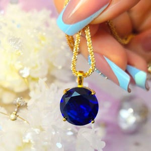May include: A gold chain necklace with a large, round, dark blue gemstone pendant.