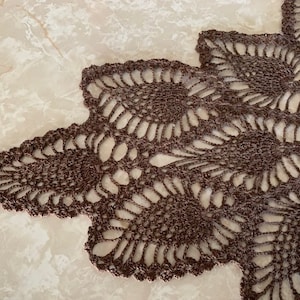 May include: A brown crocheted doily with a delicate floral pattern.