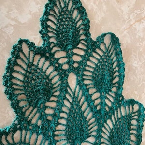 May include: A green crocheted doily with a delicate, intricate design. The doily is made of fine yarn and has a scalloped edge.