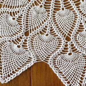 May include: White crocheted doily with a scalloped edge and a repeating pattern of circles and fans.