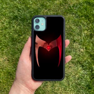 May include: Black phone case featuring a red and black graphic of a stylised eye with a red pupil. The eye is surrounded by a black shape resembling a pair of wings.