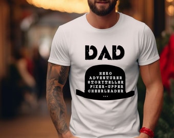 Op de afbeelding: Wit T-shirt met zwarte tekst die "DAD" zegt en een zwarte bolhoed met de woorden "HERO, ADVENTURER, STORYTELLER, FIXER-UPPER, CHEERLEADER" erin.