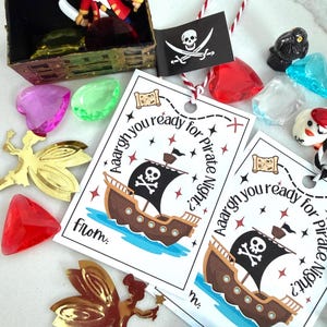 Könnte beinhalten: Eine Sammlung von Partyzubehör zum Thema Piraten. Enthält eine Schatzkiste mit einem Spielzeugpiraten, edelsteinartigen Perlen, goldenen Feenausschnitten und Etiketten mit einer Piratenschiff-Illustration und dem Text "Aargh you ready for Pirate Night?"
