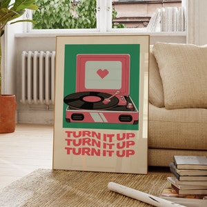 May include: A retro-style record player with a pink and green color scheme. The record player has a heart-shaped design on the front and the text "TURN IT UP" repeated three times.