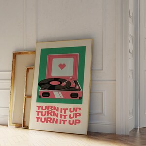 May include: A vintage-style record player with a pink body and a green background. The record player has a heart-shaped design on the front and the text "TURN IT UP" repeated three times.