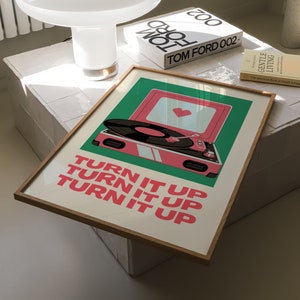 May include: A framed print with a retro-style record player on a green background. The record player is pink with a white record on it. The text "TURN IT UP" is repeated three times in pink letters.