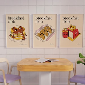 May include: Three illustrations of breakfast foods with the text "breakfast club" above each. The first illustration shows a stack of pancakes with chocolate syrup. The second illustration shows a tray of croissants. The third illustration shows a toaster with bread and jam.