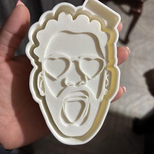 Op de afbeelding: Witte plastic koekjesvormer in de vorm van een gezicht met hartvormige zonnebrillen en een open mond.