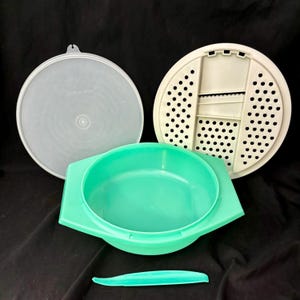 May include: A turquoise plastic bowl with a lid and a white plastic grater. The grater has a handle and a series of holes for grating food. The bowl has a small, turquoise plastic knife.