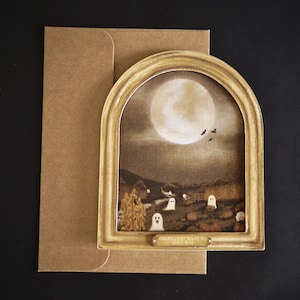 May include: A Halloween greeting card depicting a sepia-toned scene with a full moon, ghosts, and pumpkins, set within a gold-coloured arch. The card reads "Ghouls Just Want to Have Fun" and is accompanied by a brown envelope.