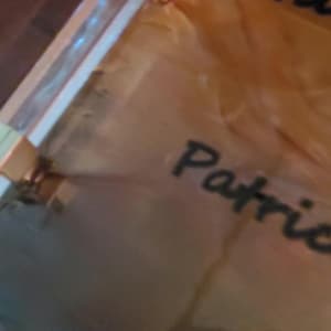Puede incluir: Un objeto parcialmente visible, transparente, de color dorado, con el nombre "Patrick" escrito en cursiva negra. La palabra "Gil" también es visible. El objeto parece ser una bolsa de regalo o un envoltorio.