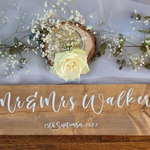 May include: Rustic wooden sign with the text "Mr & Mrs Walker" and the date "15th September 2022" in white lettering.