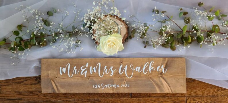 May include: Rustic wooden sign with the text "Mr & Mrs Walker" and the date "15th September 2022" in white lettering.