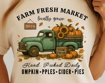 May include: Cream-colored t-shirt featuring a teal vintage truck filled with pumpkins and sunflowers. The shirt has the text "Farm Fresh Market" and "Hand Picked Daily" with the words "Pumpkin, Apples, Cider, Pies".