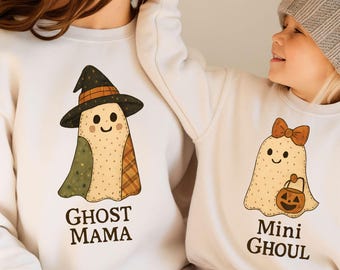 Può includere: Due felpe bianche con disegni a tema Halloween. Una presenta un fantasma con un cappello da strega e la scritta "GHOST MAMA". L'altra ha un fantasma con un fiocco e una zucca, con la scritta "Mini GHOUL".