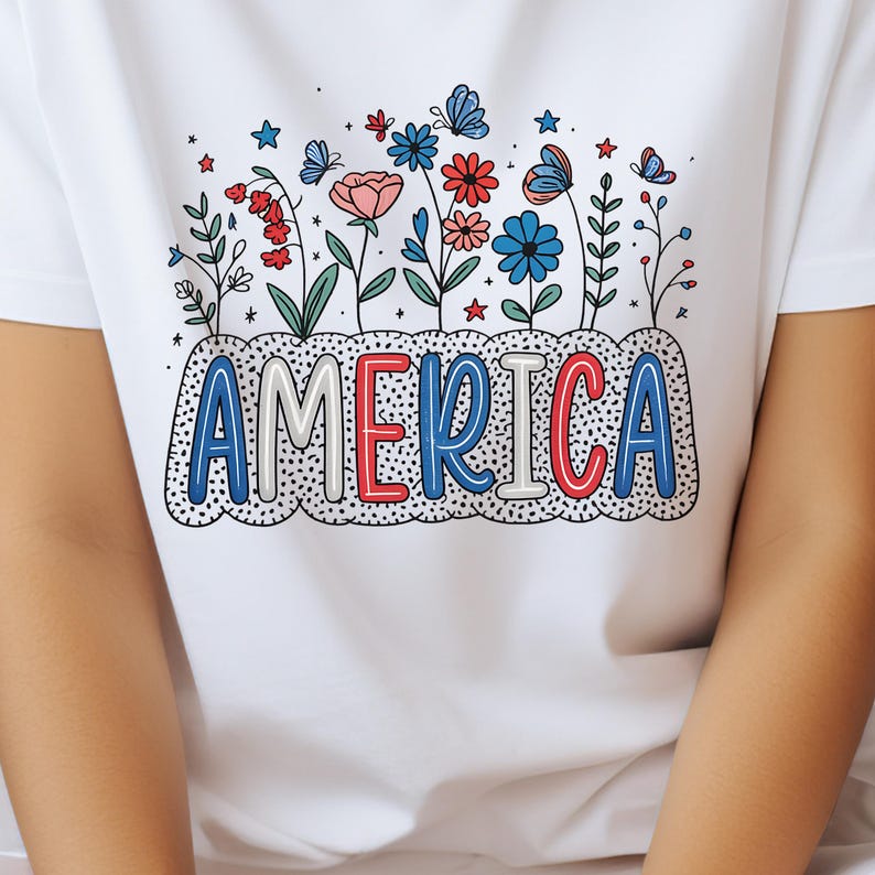 Peut inclure: T-shirt blanc avec un motif de fleurs et de papillons rouges, blancs et bleus avec le mot "AMERICA" dans une police de caract&egrave;res stylis&eacute;e.