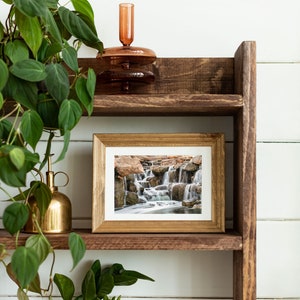 Waterfall Print wall art instant download of a soft waterfall gently flowing over the rocks in a mockup of the image framed and sitting on a shelf.