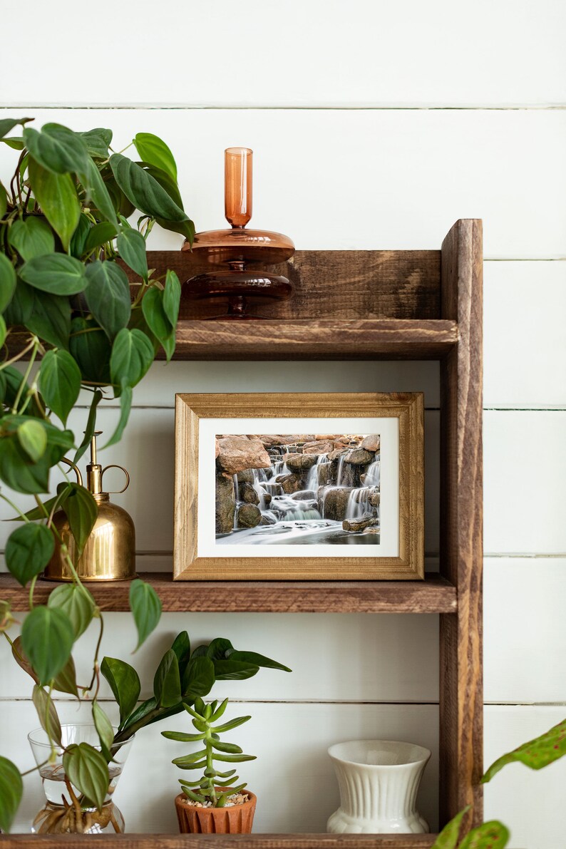 Waterfall Print wall art instant download of a soft waterfall gently flowing over the rocks in a mockup of the image framed and sitting on a shelf.