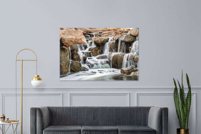 Waterfall Print wall art instant download of a soft waterfall gently flowing over the rocks in a mockup of the image printed on a metal and hanging over a sofa.