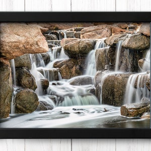 Waterfall Print wall art instant download of a soft waterfall gently flowing over the rocks in a mockup of the image in a black frame hanging on a wall.