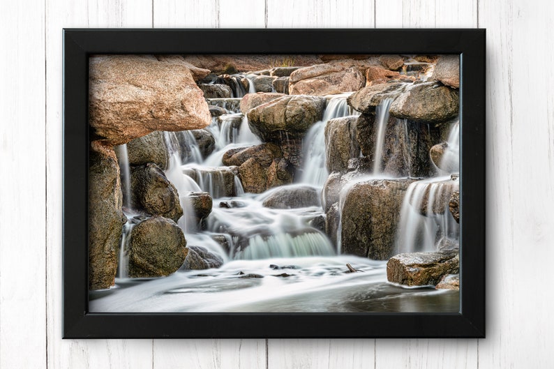 Waterfall Print wall art instant download of a soft waterfall gently flowing over the rocks in a mockup of the image in a black frame hanging on a wall.