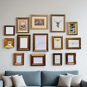 May include: An assortment of framed pictures and art pieces in decorative gold and brown frames. The frames are arranged on a light grey wall above a blue sofa with white cushions. The frames are empty or contain artwork.