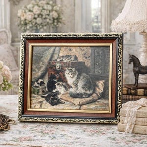 May include: A framed print showing a detailed illustration of cats. The artwork depicts a large grey cat seated on a cushion, surrounded by several kittens. The frame is brown with gold and black decorative trim, adding to the vintage aesthetic.