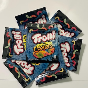 May include: Several blue and black bags of Trolli Sour Brite Crawlers candy are arranged on a white surface. The bags feature the Trolli logo and images of colorful gummy worms. The text "Sour Brite Crawlers" is visible on the bags.