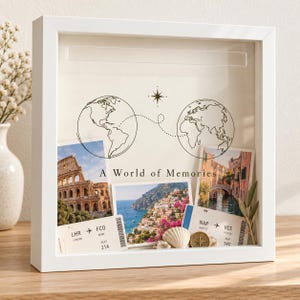 May include: A white shadow box frame containing a travel-themed display with the text A World of Memories, two globe illustrations connected by a dotted line, three photographs of Italian landmarks, two airline boarding passes, and seashells.