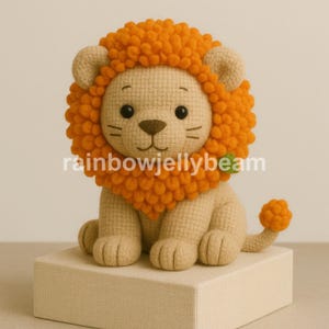 May include: A crocheted stuffed lion with a bright orange mane and a small tail. The lion is sitting on a beige surface.