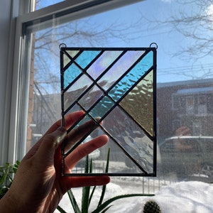 May include: A stained glass window panel with a geometric design featuring blue, green, and white iridescent glass. The panel is framed in black metal.