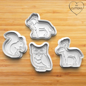 Könnte beinhalten: Vier weiße Ausstecher aus Kunststoff in Form von Waldtieren: ein Eichhörnchen, ein Fuchs, eine Eule und ein Hirsch. Die Ausstecher sind auf einer Holzoberfläche angeordnet. Der Text "MY CUTTERS" befindet sich in einem Herz.