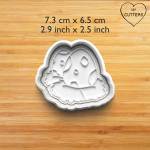 Könnte beinhalten: Weißer Plastik-Ausstecher in Form von zwei Dinosauriereiern in einem Nest. Der Ausstecher misst 7,3 cm x 6,5 cm.